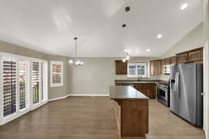 Kitchen featuring stainless steel appliances, lofted ceiling, pendant lighting, a chandelier, and a center island
