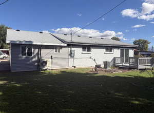 Rear view of house featuring a yard, a deck, roof with shingles, and brick siding