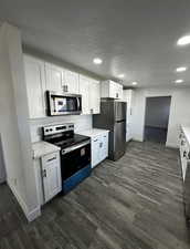 Kitchen with stainless steel appliances, a textured ceiling, white cabinetry, dark wood-style floors, and recessed lighting