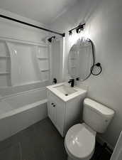 Bathroom with a textured ceiling, washtub / shower combination, vanity, and dark tile patterned floors