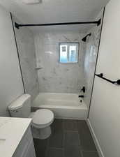 Full bath with vanity, bathing tub / shower combination, dark tile patterned flooring, and a textured ceiling