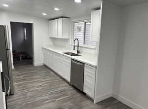 Kitchen with a textured ceiling, white cabinetry, light stone countertops, appliances with stainless steel finishes, and dark wood-type flooring
