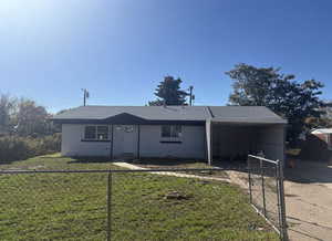 Ranch-style home featuring a fenced front yard, a carport, and roof with shingles