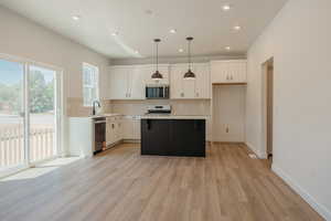 Kitchen with white cabinets, backsplash, hanging light fixtures, a kitchen island, and light wood-style floors