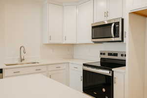 Kitchen with appliances with stainless steel finishes, white cabinets, and light stone countertops