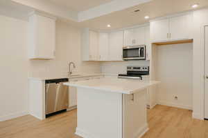 Kitchen with recessed lighting, stainless steel appliances, a kitchen island, light wood-style floors, and white cabinetry