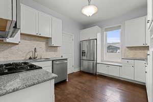 Kitchen with stainless steel appliances, white cabinets, decorative backsplash, dark wood-style flooring, and decorative light fixtures