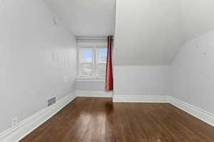Bonus room with dark wood-style floors and vaulted ceiling
