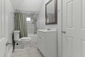 Full bath featuring shower / tub combo, vanity, vaulted ceiling, and light marble finish flooring