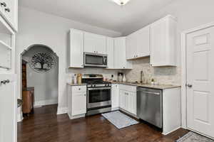 Kitchen with appliances with stainless steel finishes, white cabinetry, decorative backsplash, light stone countertops, and dark wood finished floors