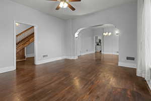 Unfurnished living room with dark wood-type flooring, ceiling fan, arched walkways, and suspended lighting