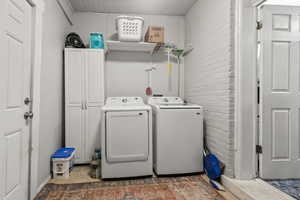 Laundry room with brick wall, light tile patterned floors, and washer and dryer