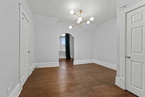 Unfurnished dining area with arched walkways, suspended lighting, dark wood-style floors, and vaulted ceiling