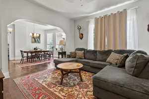 Living area featuring arched walkways, dark wood-style floors, a chandelier, and a ceiling fan