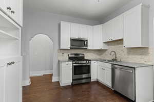 Kitchen with stainless steel appliances, white cabinets, arched walkways, and light stone countertops