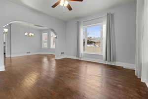 Empty room with dark wood-style floors, plenty of natural light, suspended lighting, and a ceiling fan