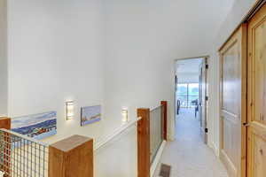 Hallway with light colored carpet and an upstairs landing