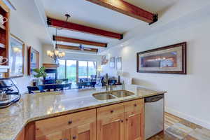 Kitchen with light stone countertops, stainless steel dishwasher, decorative light fixtures, beamed ceiling, and a ceiling fan