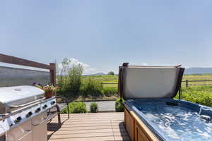 Deck with grilling area, an outdoor hot tub, a mountain view, and a rural view