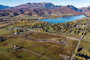 Expansive land parcel featuring partial road infrastructure, surrounded by a lake, mountains, and mature trees