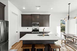 Kitchen with backsplash, stainless steel appliances, an island with sink, light wood-type flooring, and light stone countertops