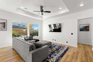 Living room featuring a tray ceiling, light wood-style flooring, recessed lighting, and ceiling fan