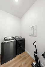 Laundry room featuring light wood-type flooring, separate washer and dryer, and electric panel
