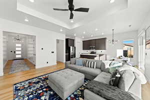Living area with a chandelier, a raised ceiling, healthy amount of natural light, light wood-type flooring, and recessed lighting