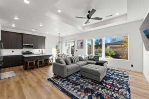 Living area featuring a tray ceiling, light wood-style floors, ceiling fan, and recessed lighting