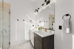 Full bathroom with double vanity, a marble finish shower, and light marble finish floors