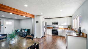 Kitchen with recessed lighting, beam ceiling, appliances with stainless steel finishes, white cabinets, and dark wood-style flooring