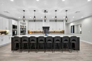 Kitchen with tasteful backsplash, a large island, a kitchen bar, white cabinetry, and recessed lighting