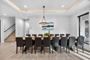 Dining room with a raised ceiling, recessed lighting, stairs, light wood-style flooring, and a chandelier