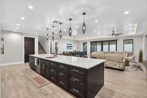 Kitchen featuring open floor plan, a large island, a raised ceiling, dark cabinets, and decorative light fixtures