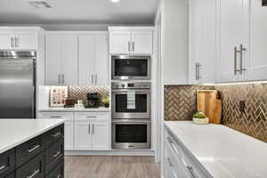 Kitchen with dark cabinets, built in appliances, white cabinets, light stone countertops, and recessed lighting