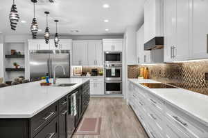 Kitchen featuring decorative light fixtures, white cabinets, backsplash, light stone counters, and built in appliances