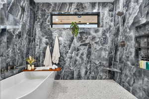 Bathroom with tile walls, a soaking tub, and a marble finish shower