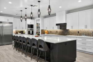 Kitchen featuring white cabinets, a large island with sink, decorative light fixtures, tasteful backsplash, and built in appliances