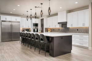 Kitchen featuring white cabinets, a large island, a breakfast bar, built in appliances, and decorative light fixtures