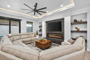 Living area with built in features, a tray ceiling, a fireplace, a ceiling fan, and recessed lighting