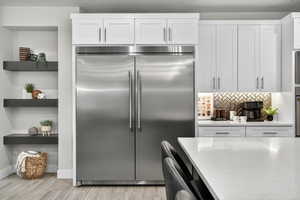 Kitchen featuring stainless steel built in refrigerator, white cabinets, backsplash, and light stone counters