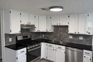 Kitchen with stainless steel appliances, white cabinetry, a textured ceiling, decorative backsplash, and light tile patterned floors