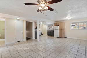 Unfurnished living room featuring a textured ceiling, light tile patterned floors, and ceiling fan
