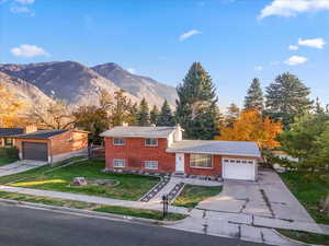 Tri-level home with an attached garage, driveway, a chimney, a front lawn, and a mountain view