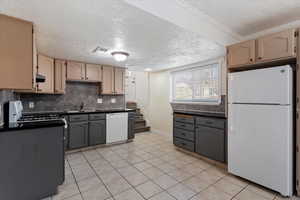 Kitchen with white appliances, dark countertops, gray cabinetry, light tile patterned floors, and a textured ceiling