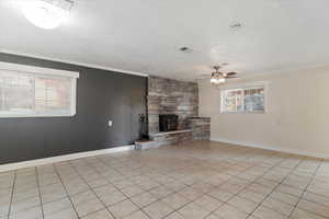 Unfurnished living room featuring ornamental molding, a textured ceiling, light tile patterned floors, ceiling fan, and a stone fireplace
