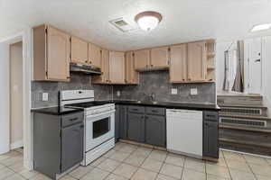 Kitchen with white appliances, backsplash, light tile patterned floors, a textured ceiling, and under cabinet range hood