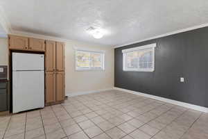Kitchen featuring freestanding refrigerator, light brown cabinetry, light tile patterned floors, ornamental molding, and a textured ceiling