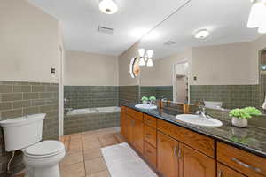 Bathroom featuring double vanity, light tile patterned floors, a bath, tile walls, and wainscoting