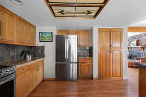 Kitchen featuring stainless steel appliances, dark wood-style floors, a textured ceiling, brown cabinetry, and backsplash